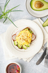 Plate with tasty scrambled eggs sandwich and vegetables on light background