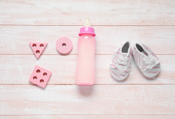 Bottle of milk for baby with toys and booties on pink wooden background