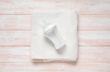 Bottle of milk for baby with towel on wooden pink background