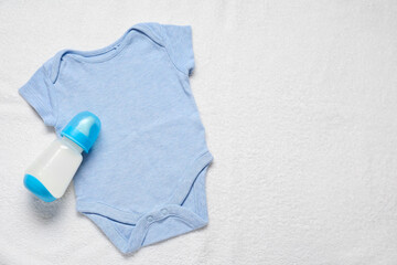 Bottle of milk for baby and bodysuit on white towel