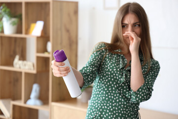 Displeased young woman with air freshener at home