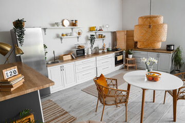 Interior of light kitchen with stylish fridge, counters, lamp, table and chairs