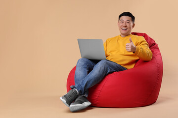 Emotional man with laptop showing thumb up gesture on beige background, space for text