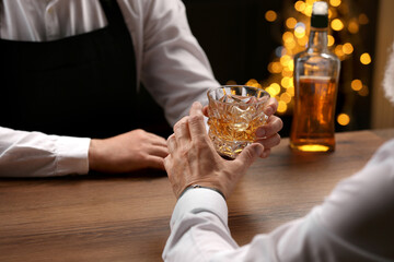 Bartender giving glass of whiskey to customer at bar counter, closeup