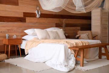 Fototapeta na wymiar Interior of modern bedroom with bed, bench and dream catcher hanging on wooden wall