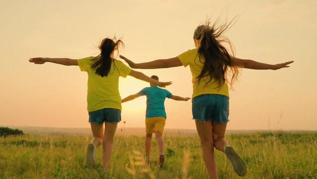 Children play in pilot park. Boy, girls, arms outstretched, run through green grass. Family of children run on meadow at sunset. Happy children run in nature. Concept freedom. Funny kids playing pilot