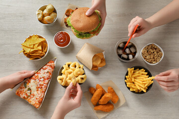 Friends eating french fries, burger and other fast food at white wooden table, top view
