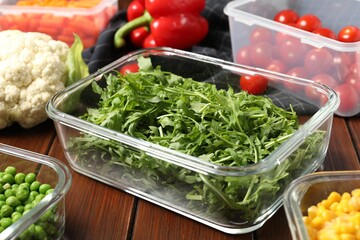Containers with arugula and fresh products on wooden table, closeup. Food storage