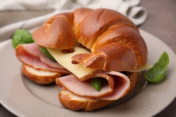Tasty crescent roll with ham, cheese and basil on plate, closeup