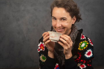 Mujer joven sonriente, con ropa de invierno, tomando té