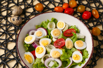 Tasty salad with quail eggs, tomatoes, onion and lettuce on beige background, closeup
