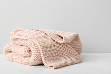 New knitted folded blanket on table near light wall