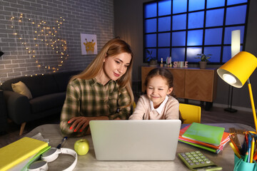 Little girl with her mother doing lessons at home late in evening