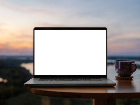 Laptop blank screen on wood table with amazing sunset sky over river mockup.Clipping path device screen. Front view of silver aluminium laptop near panoramic windows with summer nature country view