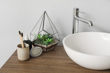 Table with sink bowl, toothbrushes and florarium in bathroom