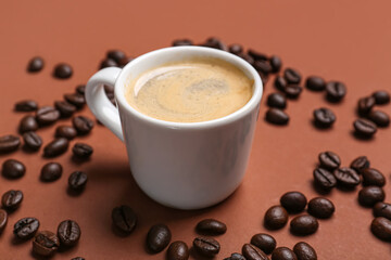 Cup of hot espresso and coffee beans on brown background