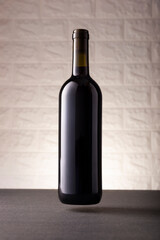Unlabeled red wine bottle mockup floating on gray stone surface, white rustic brick wall background. Minimalist concept.