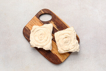 Wooden board of tasty toasts with cream cheese on light background