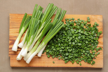 Board with slices of fresh green onion on brown background