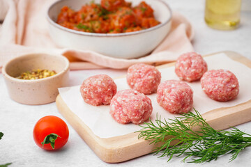 Wooden board with raw meat balls on light background