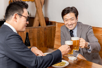 居酒屋で同僚・友達と飲み会・ビールで乾杯をするスーツ姿のビジネスマン・サラリーマンの男性
