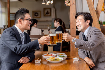 居酒屋で同僚・友達と飲み会・ビールで乾杯をするスーツ姿のビジネスマン・サラリーマンの男性
