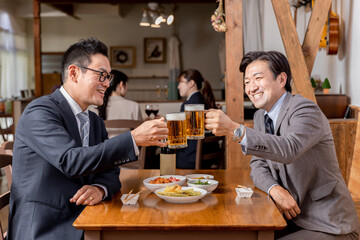 居酒屋で同僚・友達と飲み会・ビールで乾杯をするスーツ姿のビジネスマン・サラリーマンの男性
