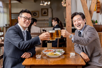 居酒屋で同僚・友達と飲み会・ビールで乾杯をするスーツ姿のビジネスマン・サラリーマンの男性
