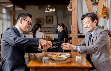 飲み会・接待・親睦会で上司や同僚にお酌する笑顔のビジネスマン
