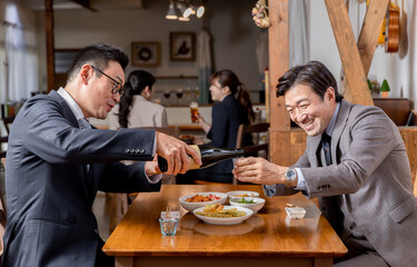 飲み会・接待・親睦会で上司や同僚にお酌する笑顔のビジネスマン
