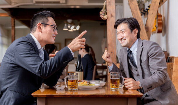 居酒屋で酒・ビールを飲みながら同僚・友達と楽しく会話するビジネスマン
