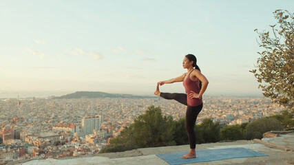 Girl practices yoga stands on one leg at lookout point at dawn