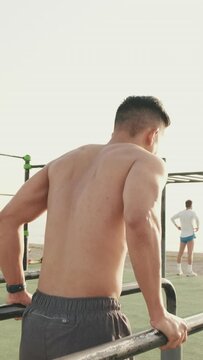 Young man doing push-ups on parallel bars on a sports ground by the sea
