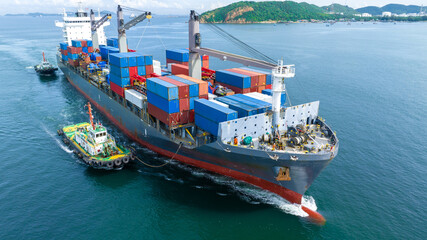 Aerial front view of cargo ship carrying container and running with tug boat for import export...