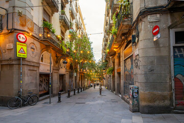 A narrow alley through a picturesque section of the Gothic Quarter with lights illuminated the street at twilight in Barcelona, Spain.