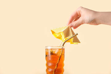 Woman decorating glass of ice tea with umbrella on beige background