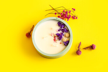 Holder with candle and flowers on yellow background