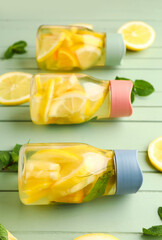 Sports bottles of infused water with lemon and mint on green wooden background