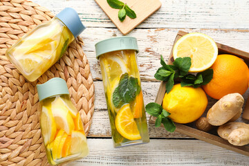 Sports bottles of infused water and box with different citrus fruits on white wooden background