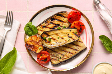 Plate with delicious grilled eggplants, tomatoes and garlic on pink background, top view