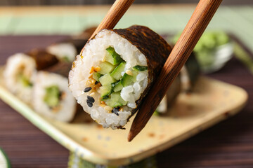 Chopsticks with tasty maki roll, closeup view