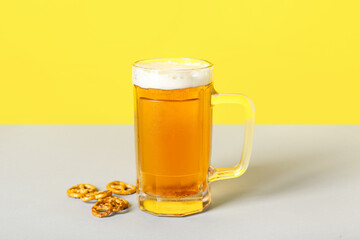 Mug of cold beer and pretzels on color background