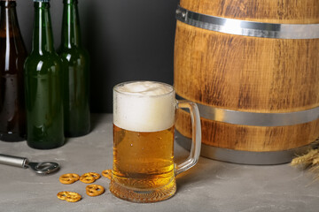 Mug of cold beer, wooden barrel and pretzels on table