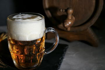Mug of cold beer and wooden barrel on table, closeup
