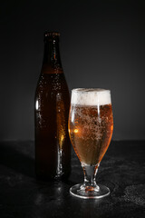 Bottle and glass of cold beer on dark background