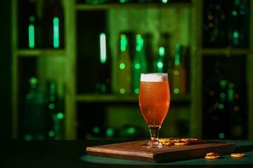 Glass of fresh beer with pretzels on table in bar