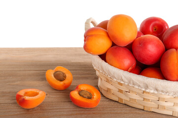 Wicker basket with ripe apricots on table against white background
