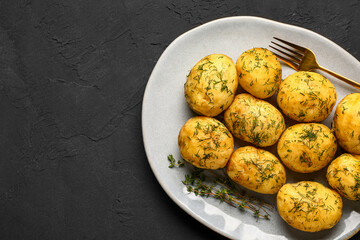 Plate of boiled baby potatoes with dill on black background