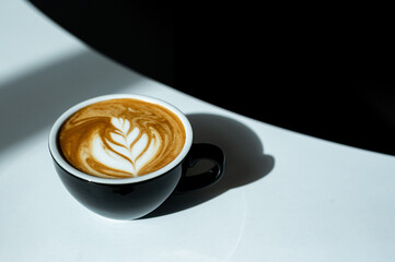 Coffee cup with latte art on white table with black background