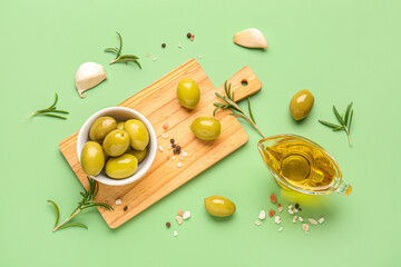 Bowl with ripe olives and gravy boat of oil on green background